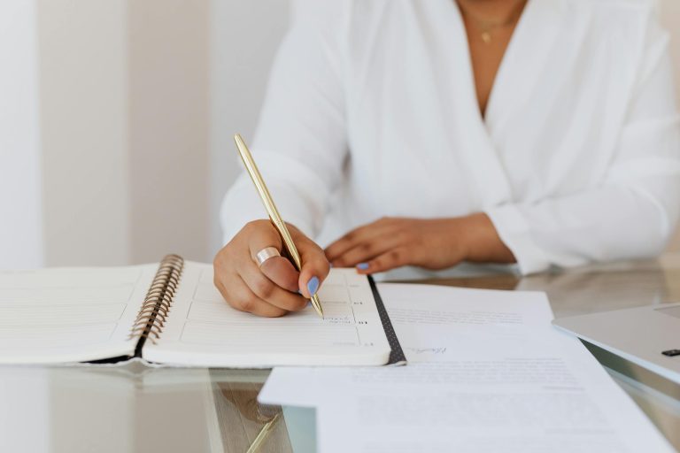 Close-up of a person writing notes in a planner with a gold pen, emphasizing organization.